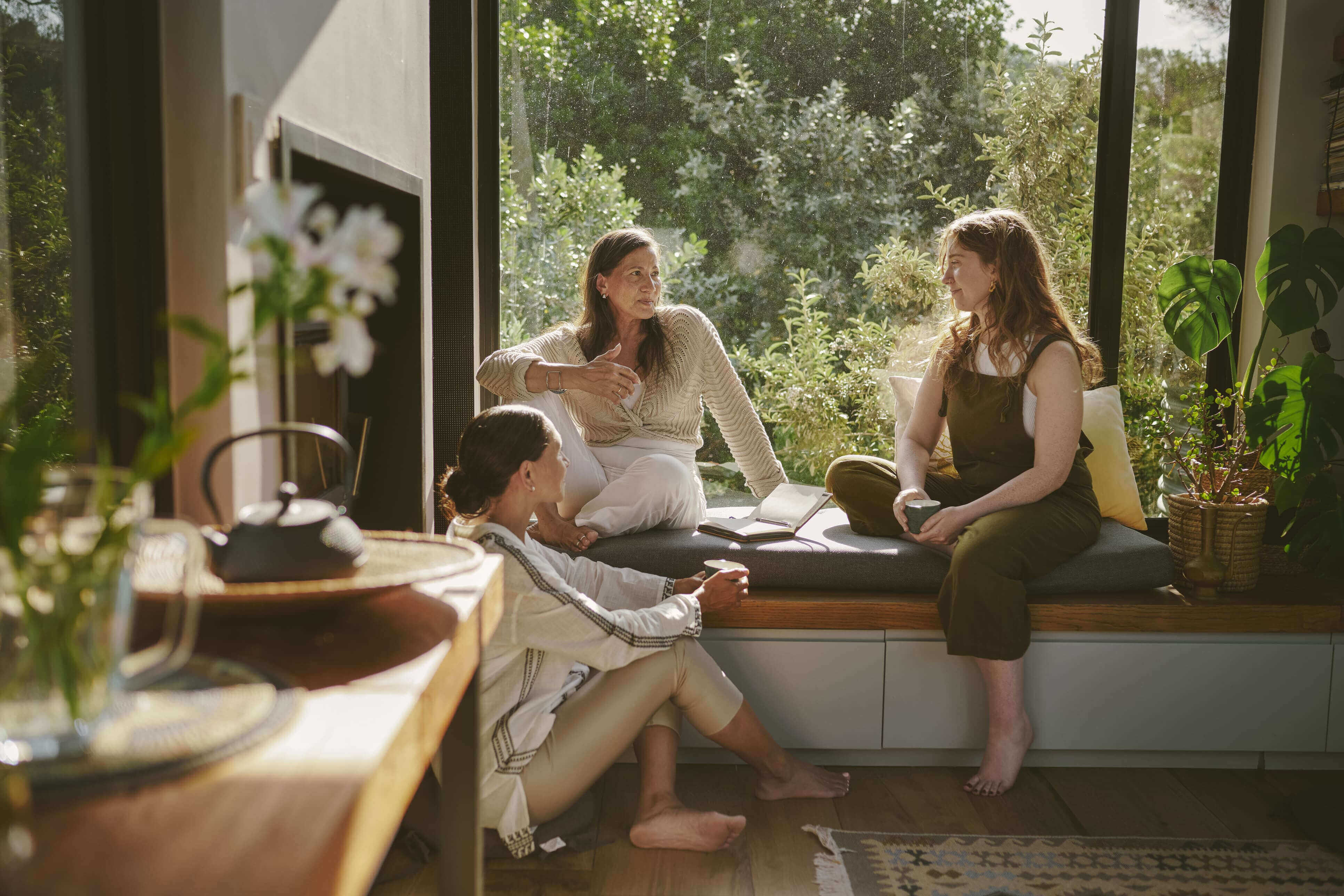 Three women sitting by a large window having a relaxed conversation
